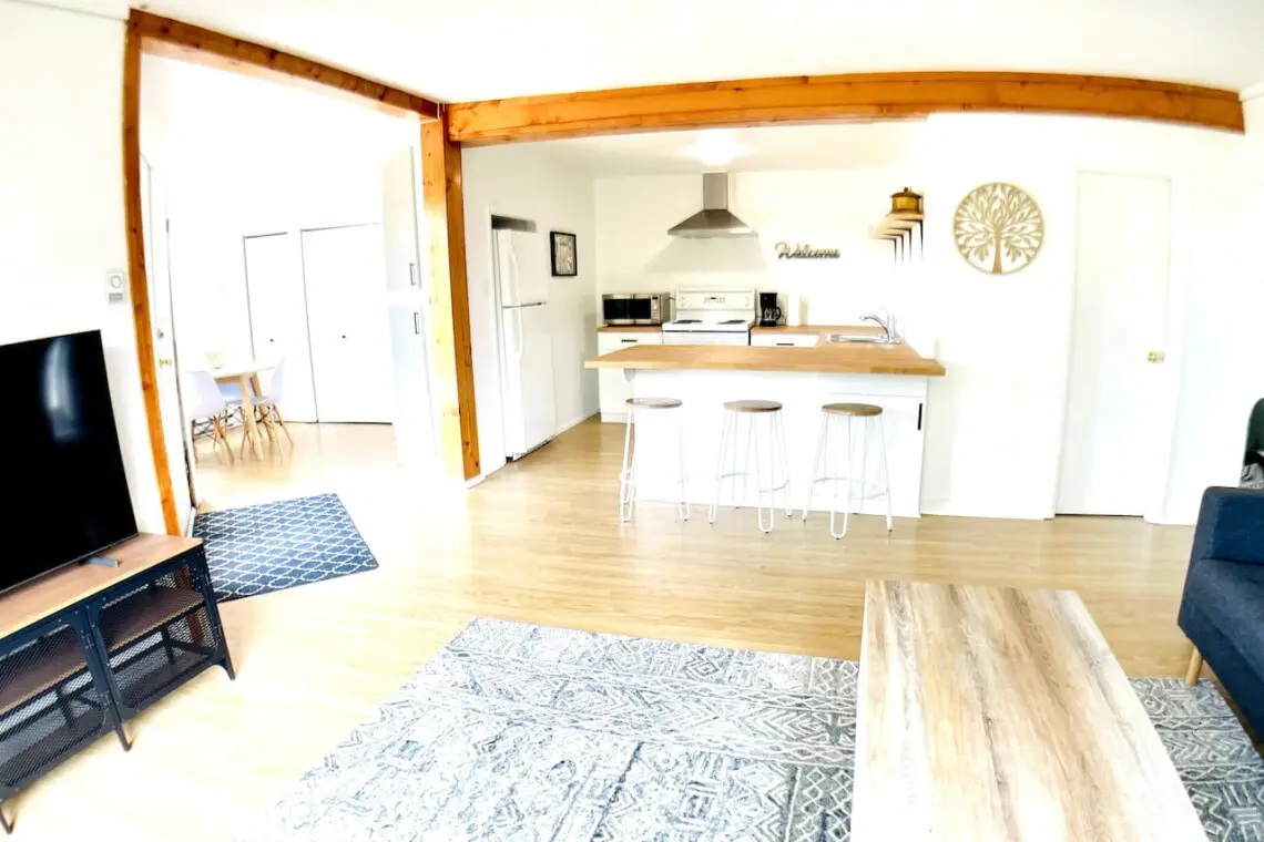 An open living and kitchen space with a breakfast bar, wooden accents, and bright natural light throughout.