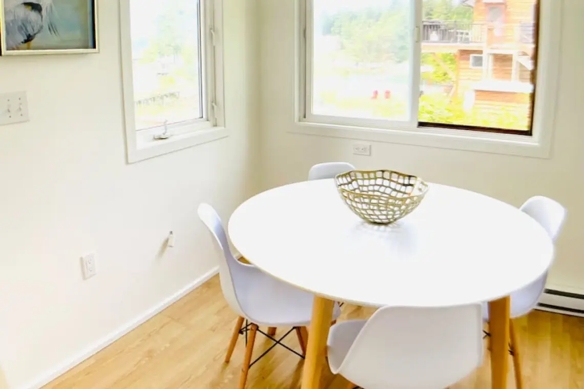 Bright dining nook with a minimalist round table, modern chairs, and large windows offering natural light and peaceful views.