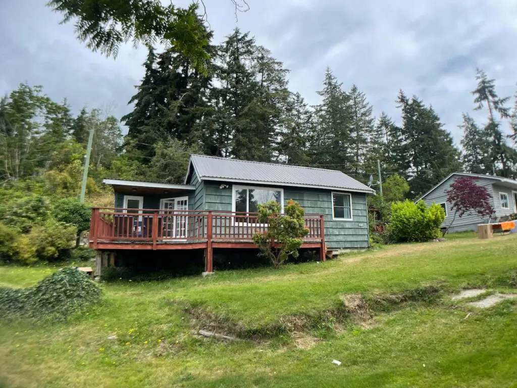 Cozy cottage surrounded by trees with a spacious deck, offering a peaceful retreat in a lush, green setting.