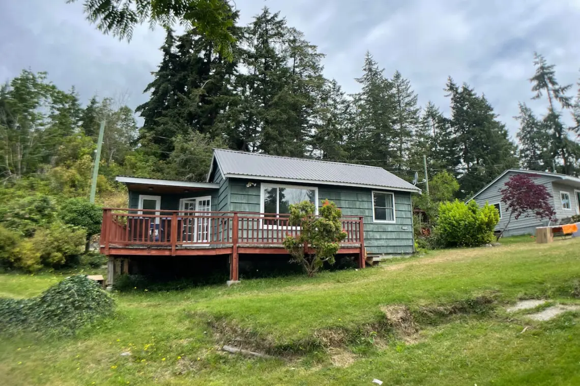 Cozy cottage surrounded by trees with a spacious deck, offering a peaceful retreat in a lush, green setting.