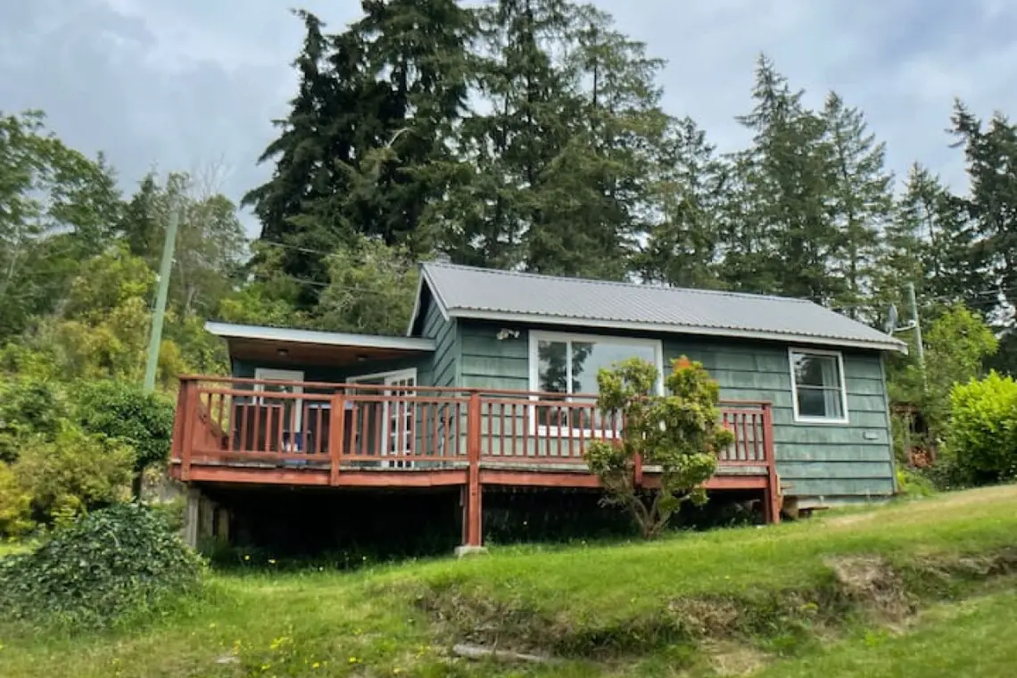 Charming cottage nestled among trees, with a spacious deck offering a serene retreat surrounded by lush greenery.