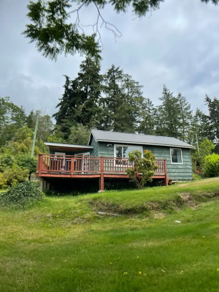 Charming cottage nestled among trees, with a spacious deck offering a serene retreat surrounded by lush greenery.