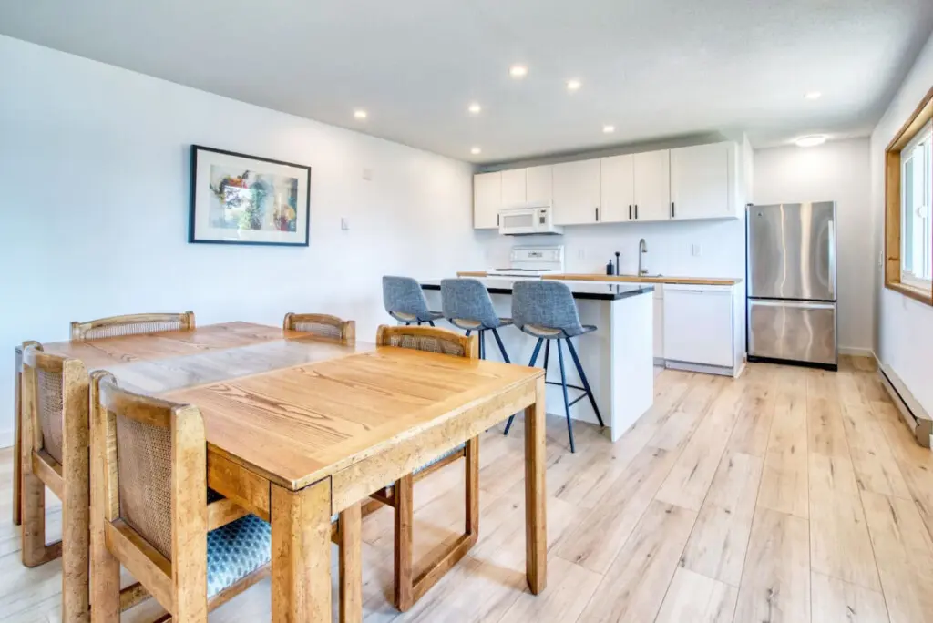 Open dining and kitchen space with a wooden dining table, three bar stools at the black countertop island, and modern appliances for convenient cooking and socializing.
