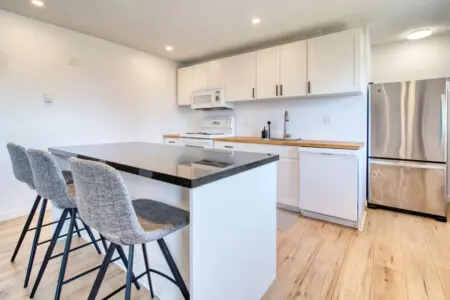 Sleek modern kitchen featuring a black countertop island, three cushioned bar stools, stainless steel appliances, and ample cabinet space for meal prep and casual dining.
