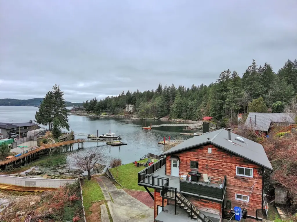 Scenic aerial view of a waterfront property with a wooden home, private dock, and lush forest surroundings, perfect for a peaceful retreat.
