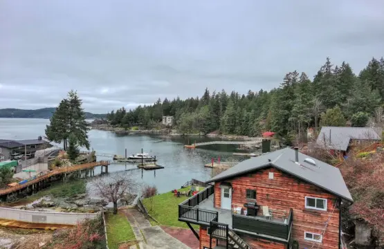 Scenic aerial view of a waterfront property with a wooden home, private dock, and lush forest surroundings, perfect for a peaceful retreat.