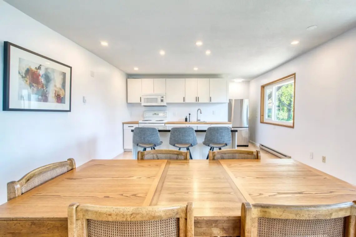 Bright open-concept kitchen and dining area with a wooden dining table, modern bar seating, and stainless steel appliances for convenient meal preparation.