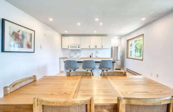 Bright open-concept kitchen and dining area with a wooden dining table, modern bar seating, and stainless steel appliances for convenient meal preparation.