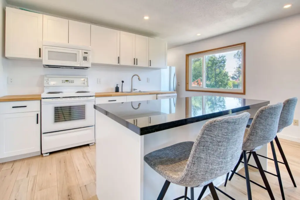 Modern kitchen with a sleek black countertop island, three upholstered bar stools, and full appliances for convenient cooking and casual dining.