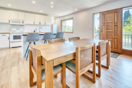 Open dining and kitchen space with a wooden dining table, three bar stools at the black countertop island, and modern appliances for convenient cooking and socializing.